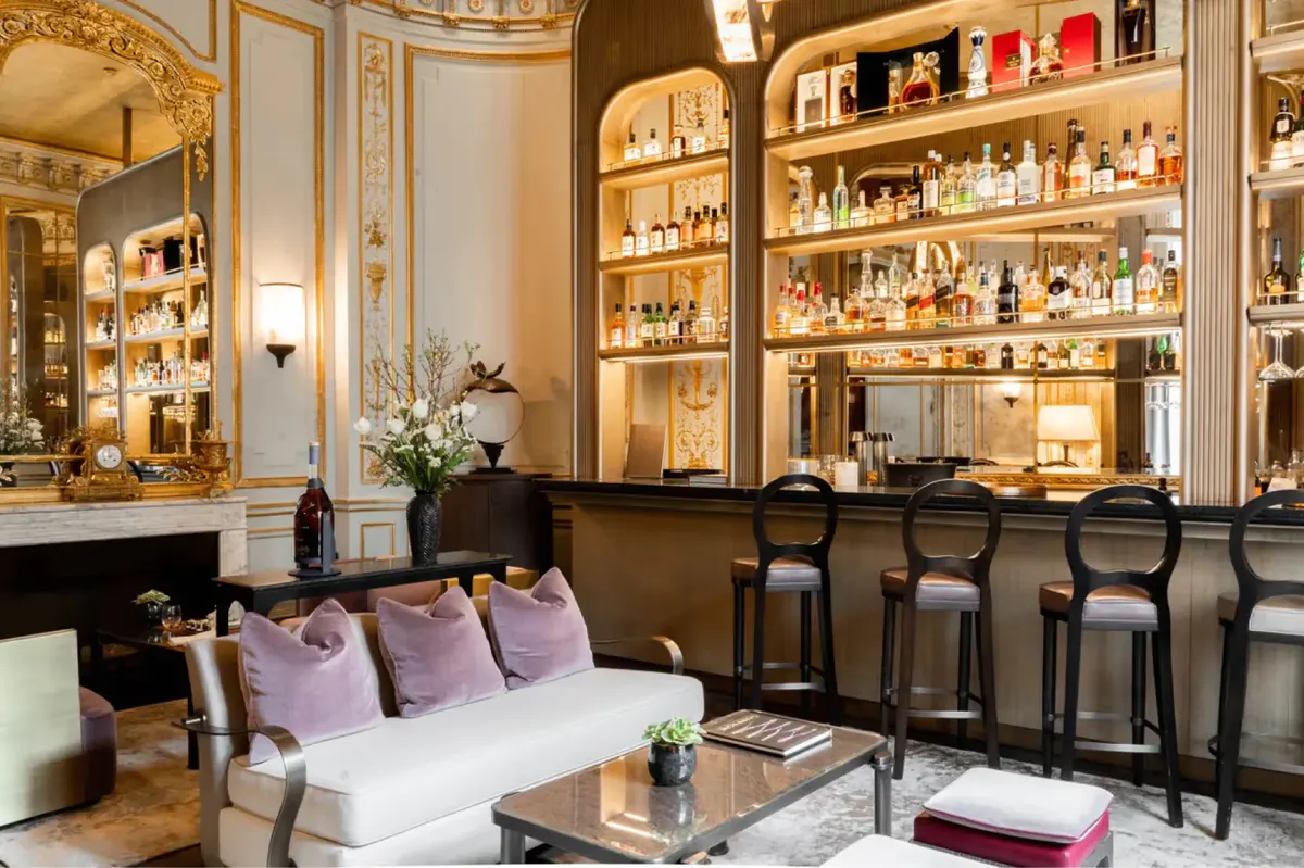 A bar lounge with illuminated glass cabinets, bar counter with stools, and ornate gold details