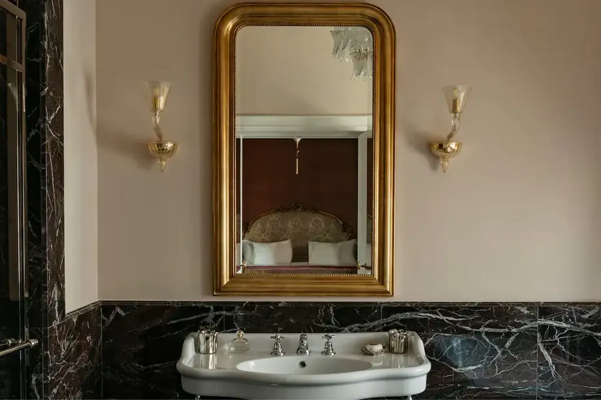 An ornate gold-framed mirror above a marble sink with slate wall panels
