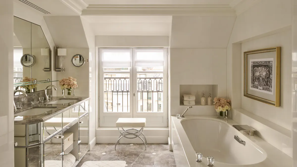 A marble bathroom with vanity, curved windows framing the city view, and a soaking tub