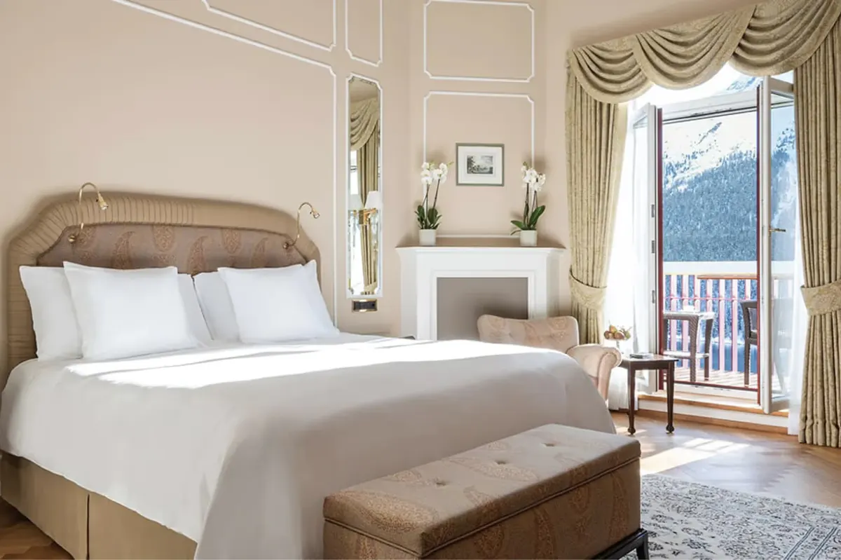 Bedroom with upholstered headboard, white linens, balcony with lake view