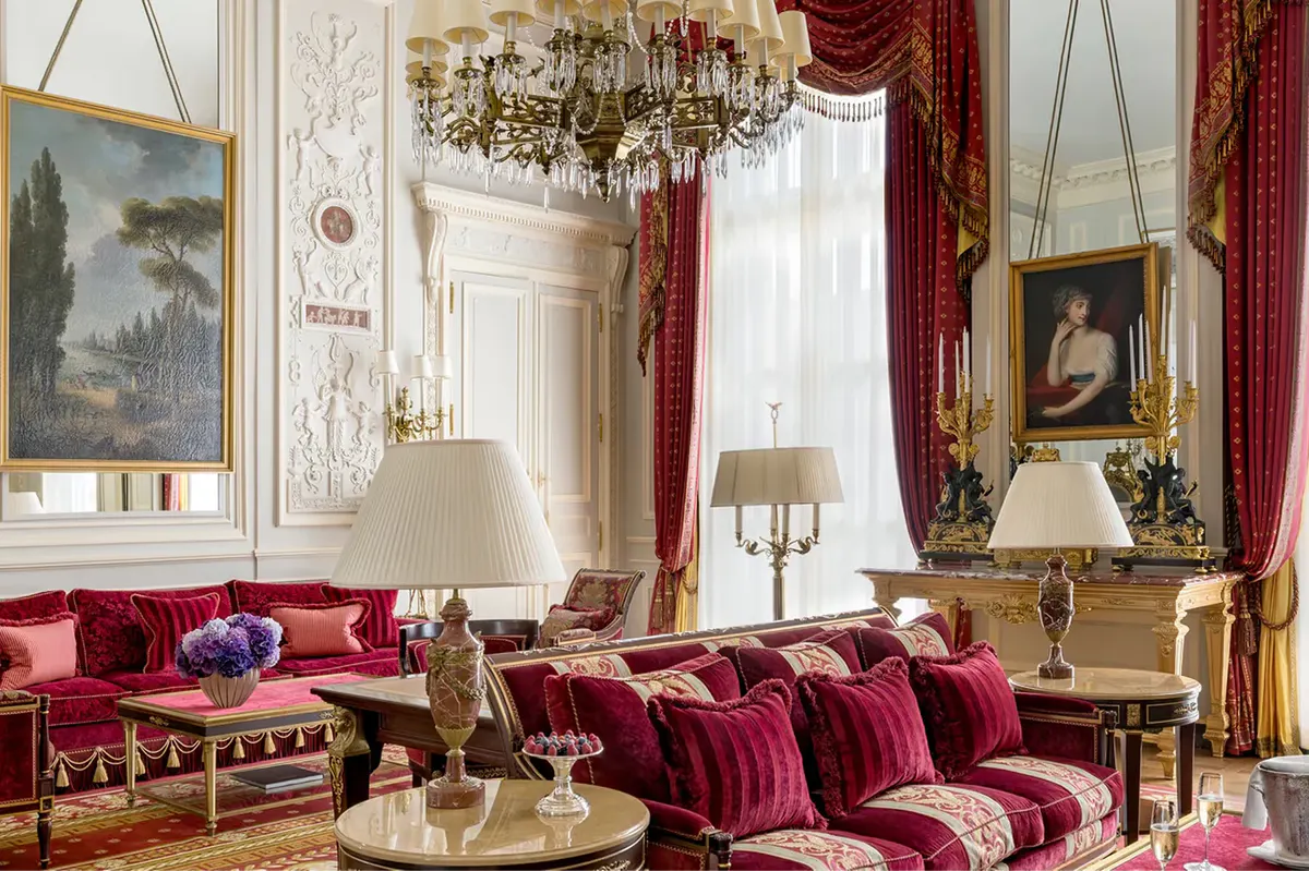 A salon with red velvet furnishings, gilt mirrors, and ornate ceiling moldings