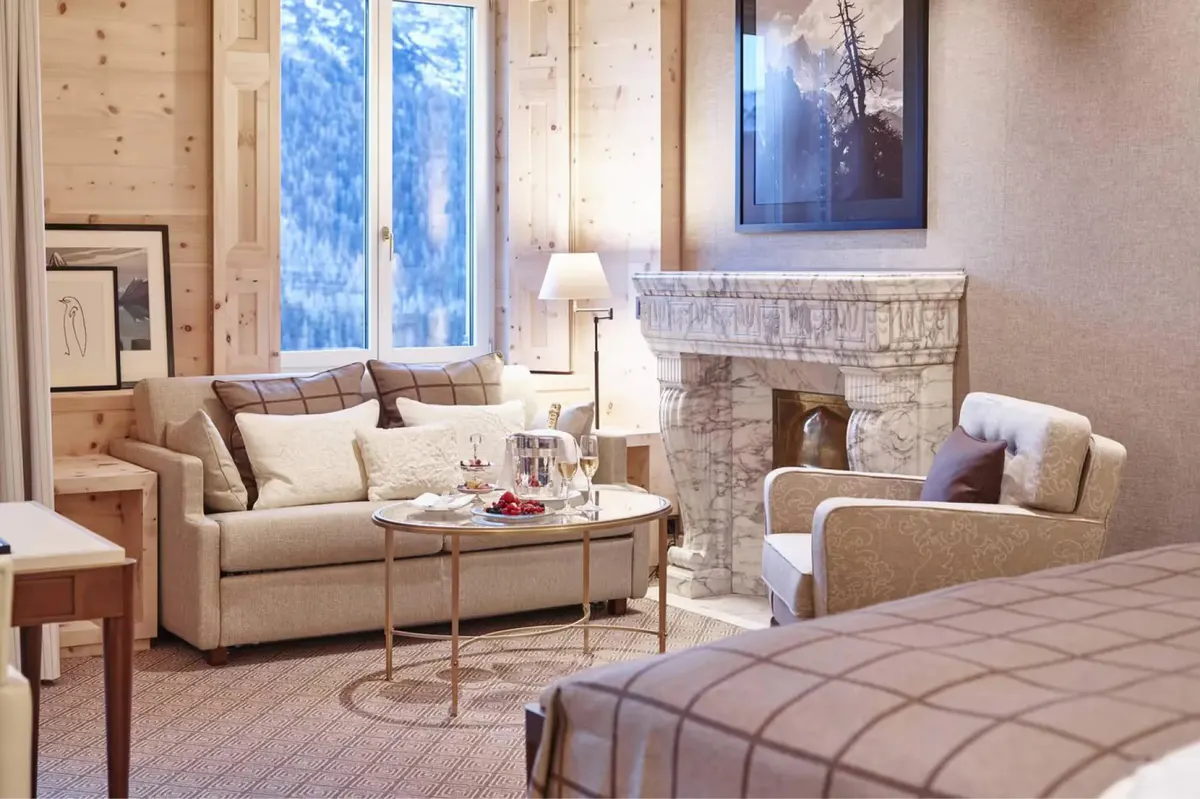 A suite with a sofa and fireplace, framing a snowy Alpine landscape