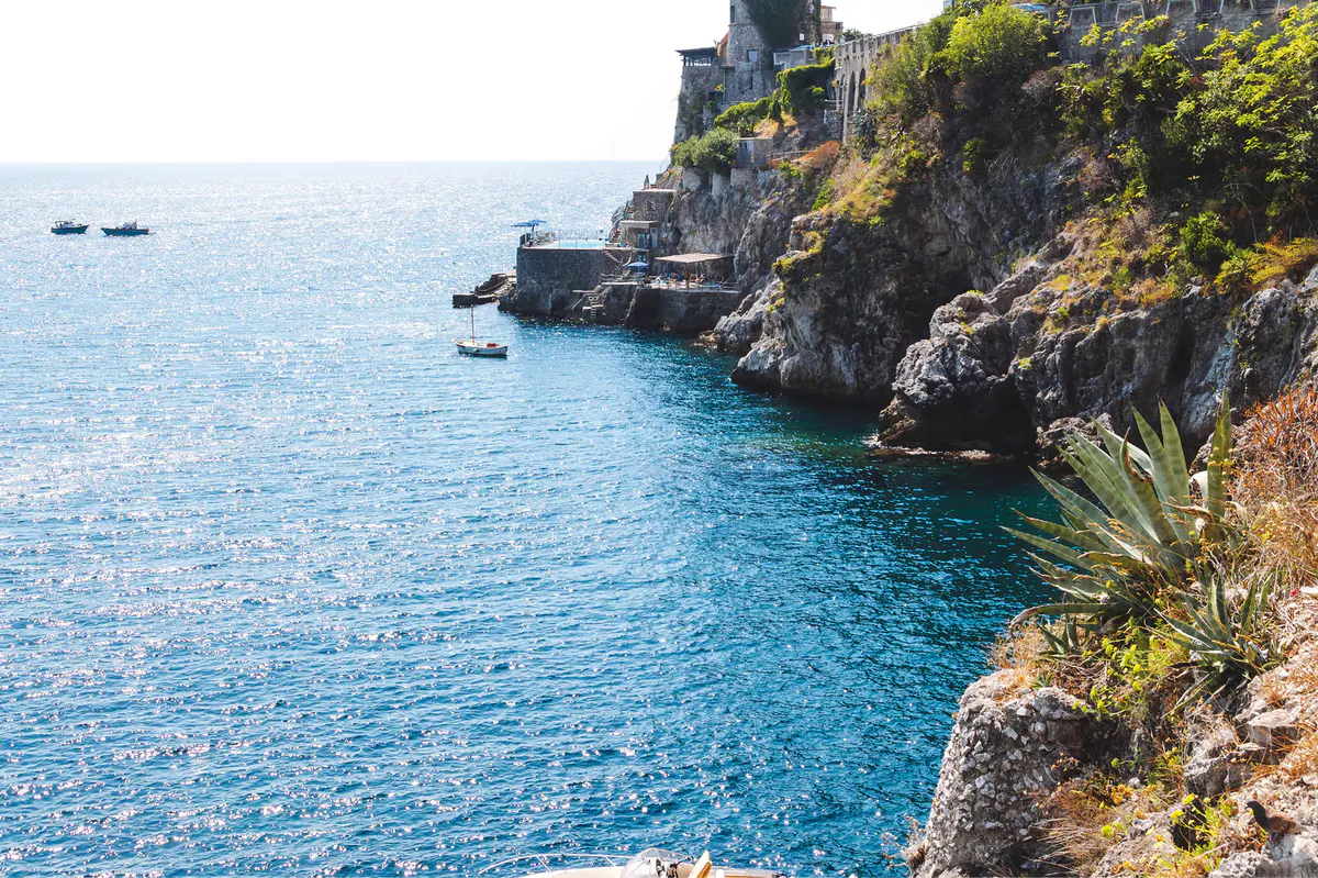 Rocky coastal outcrop with terraced white buildings cascading down cliff to turquoise water