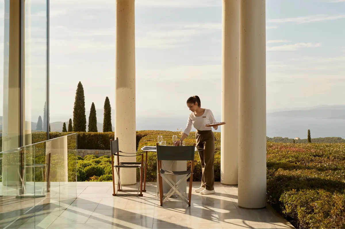 Server pouring wine at a columned restaurant overlooking the sea