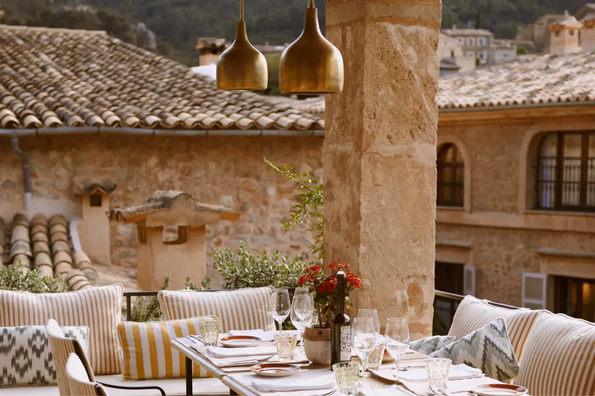 Courtyard dining area with natural stone walls, hanging pendant lights, and rustic wooden furnishings