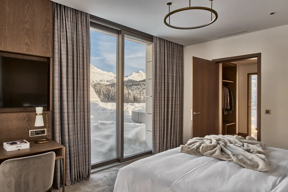 Bedroom with brown wood accents, tan bedding, glass doors opening to balcony views