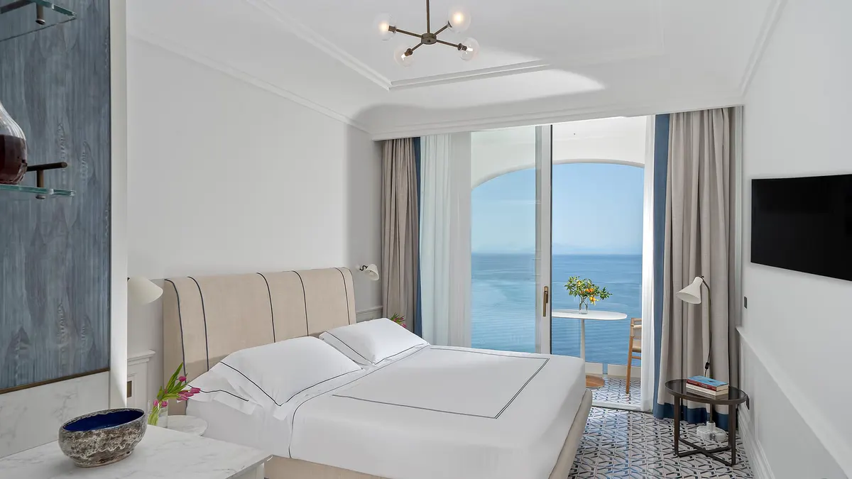 Modern suite with upholstered headboard, ocean-facing balcony, and soft neutral tones