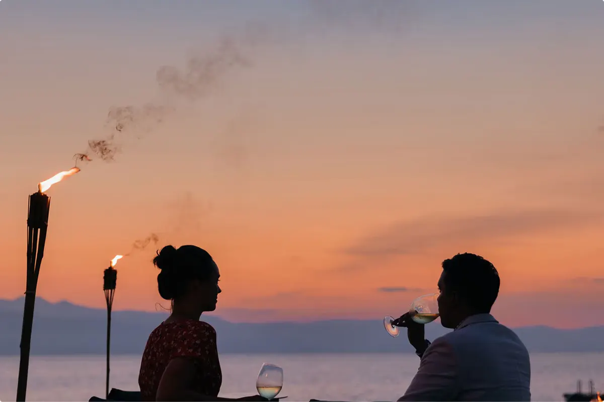 Couple dining at sunset with torch lighting and bay views