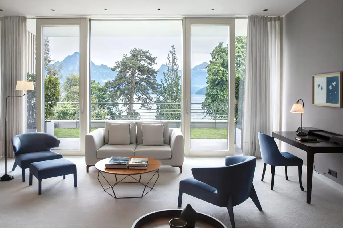 Modern sitting area with large windows, gray sofa, wood accent table, and Alpine views