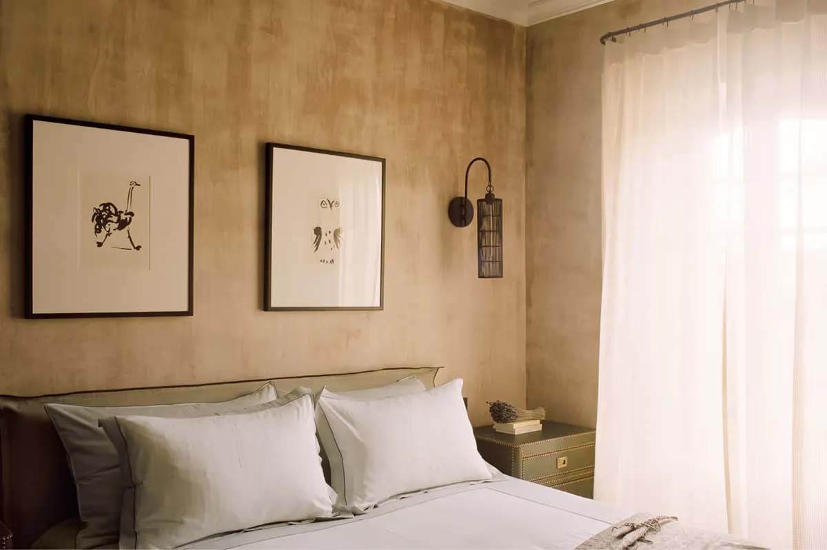 Bedroom with taupe upholstered headboard, framed prints on wall, and soft lighting