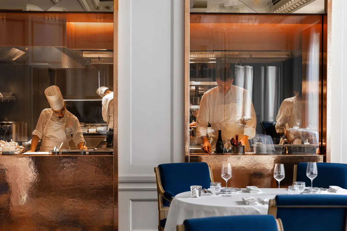 A dining room with display cases, blue velvet chairs, and elegant table service