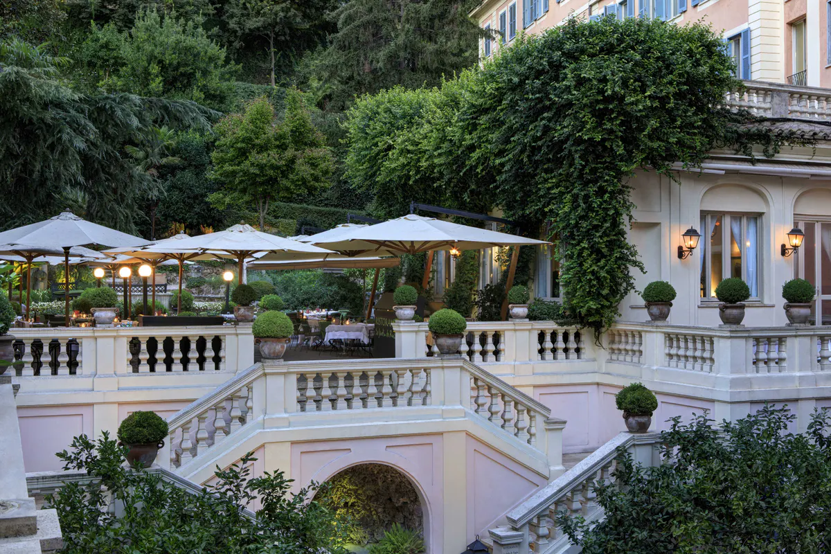 Tiered garden terrace with beige umbrellas, balustrade, and lush greenery