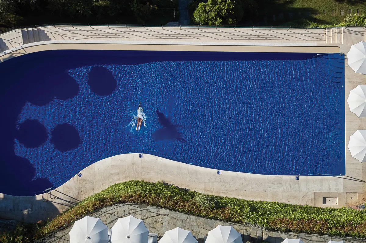 An aerial view of the infinity pool with swimmers, surrounded by green lawns