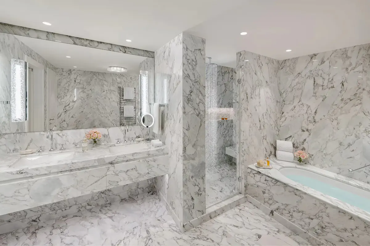 Modern bathroom with marble surfaces, walk-in shower, and dual vanities