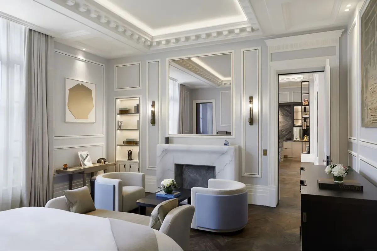 A suite with pale color palette, central fireplace, seating area, and ornate ceiling molding