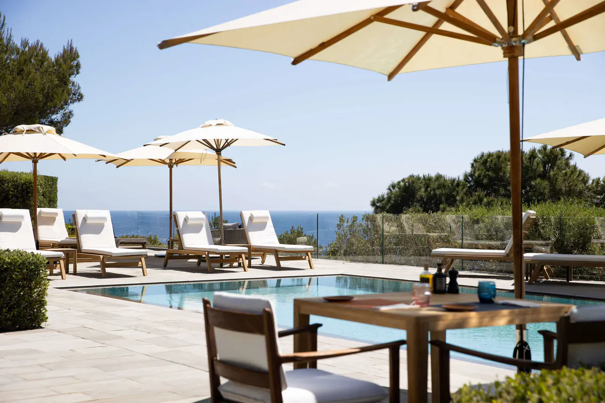 Pool with white lounges and tables beneath wooden umbrellas