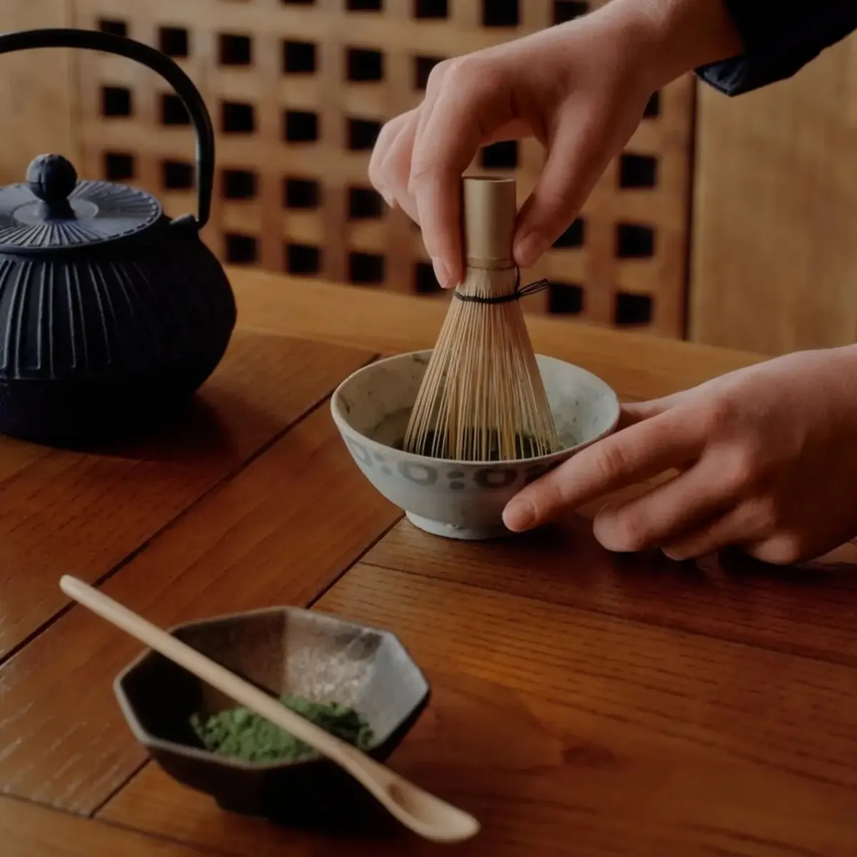 Japanese tea ceremony with a bamboo whisk stirring matcha beside a cast iron teapot