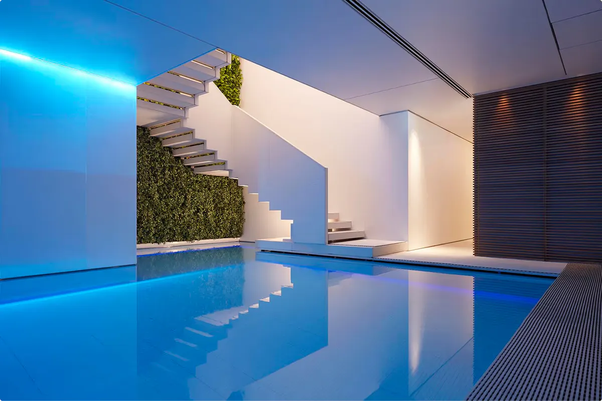 Illuminated swimming pool with blue water, modern white columns, and spa area