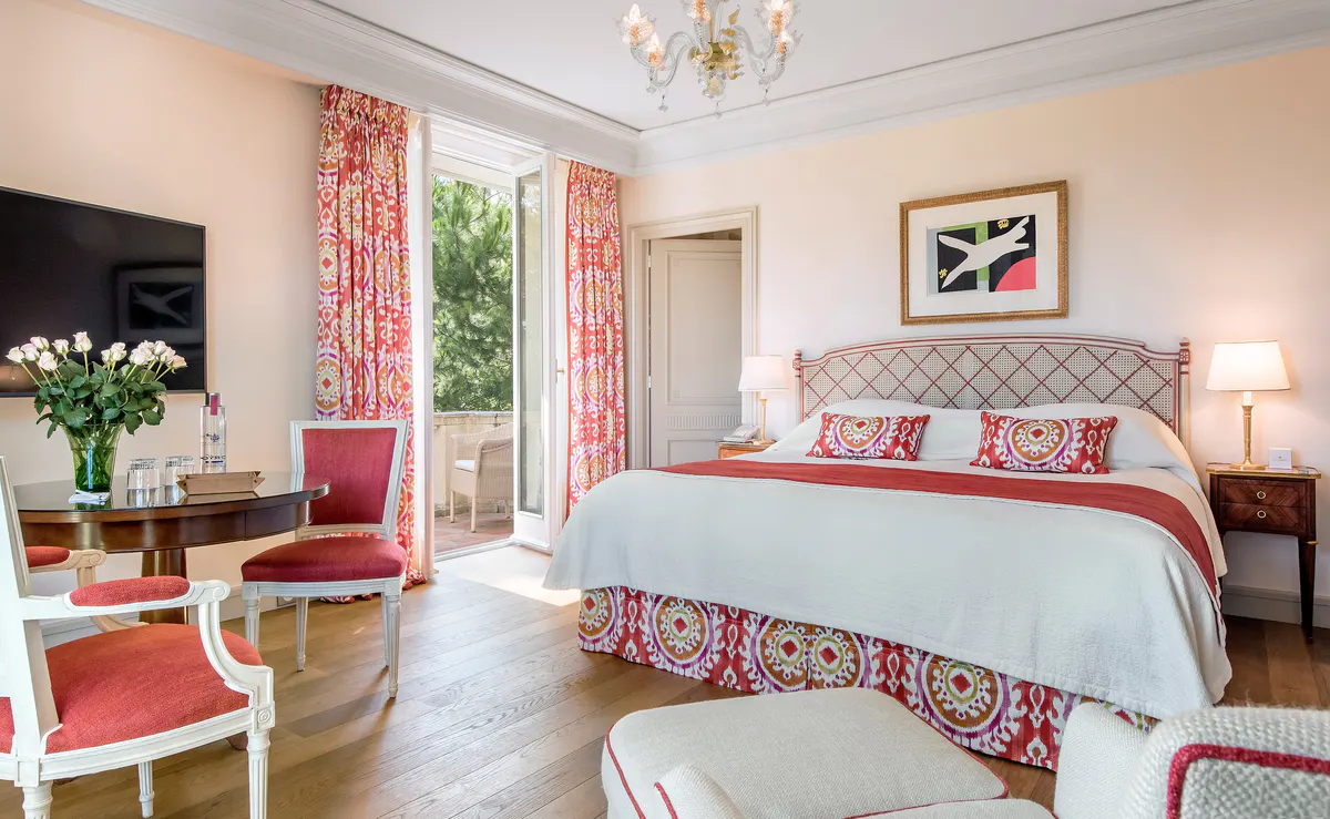 A bedroom with coral and white décor, matching bed covers, patterned curtains, and fresh flowers