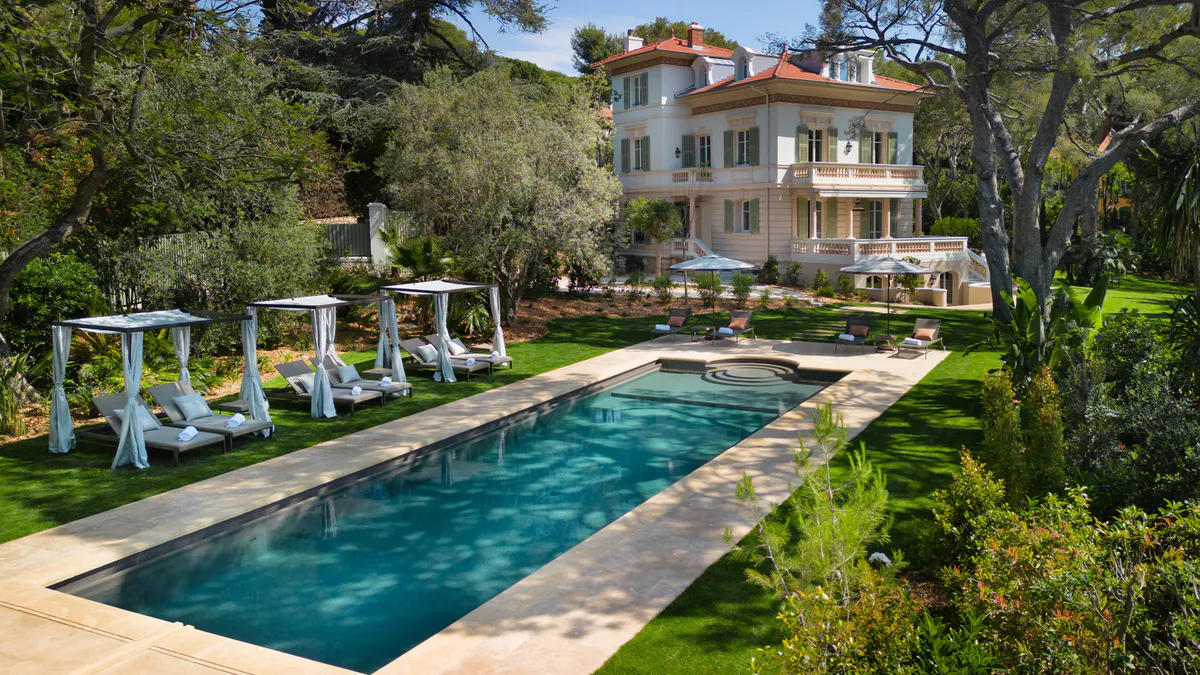 Terracotta villa with pool and white lounge chairs in gardens