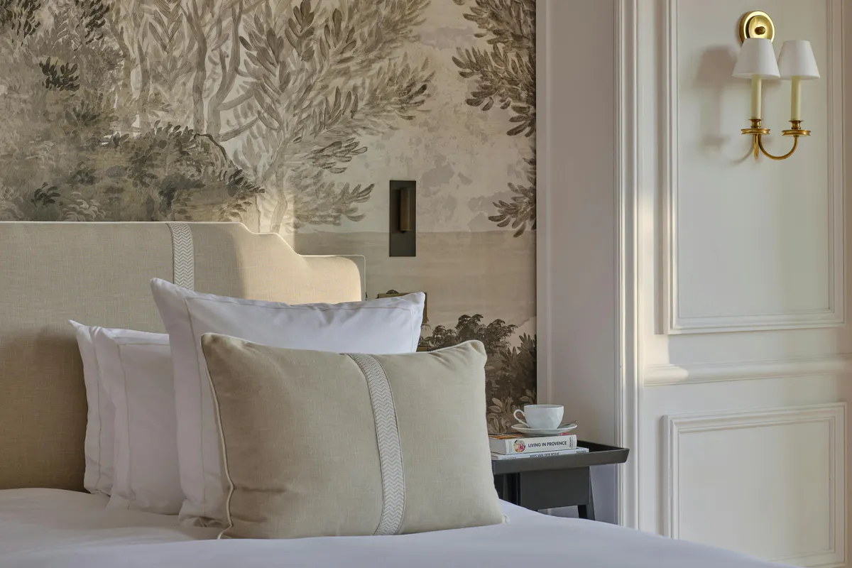 Bedroom with paneled headboard wall, white linens, and gold wall sconces