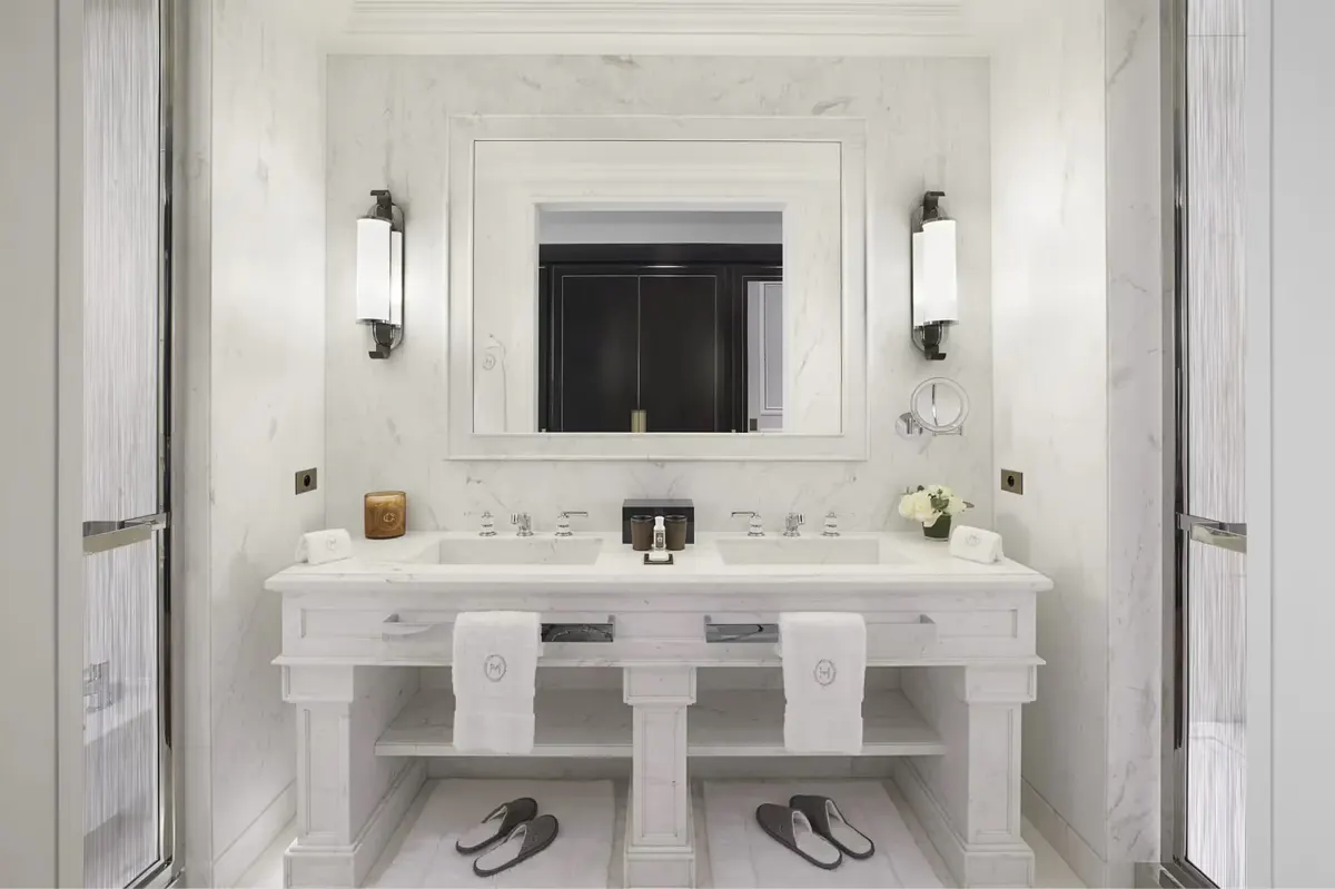 A marble bathroom with white twin vanities, large mirror, white sconces, and clean minimalist design