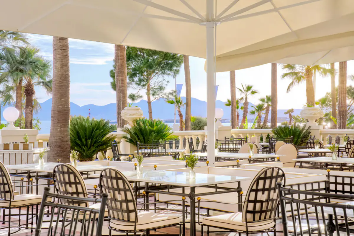 Terrace dining area under white umbrellas with sea views, palm trees, and woven dining chairs
