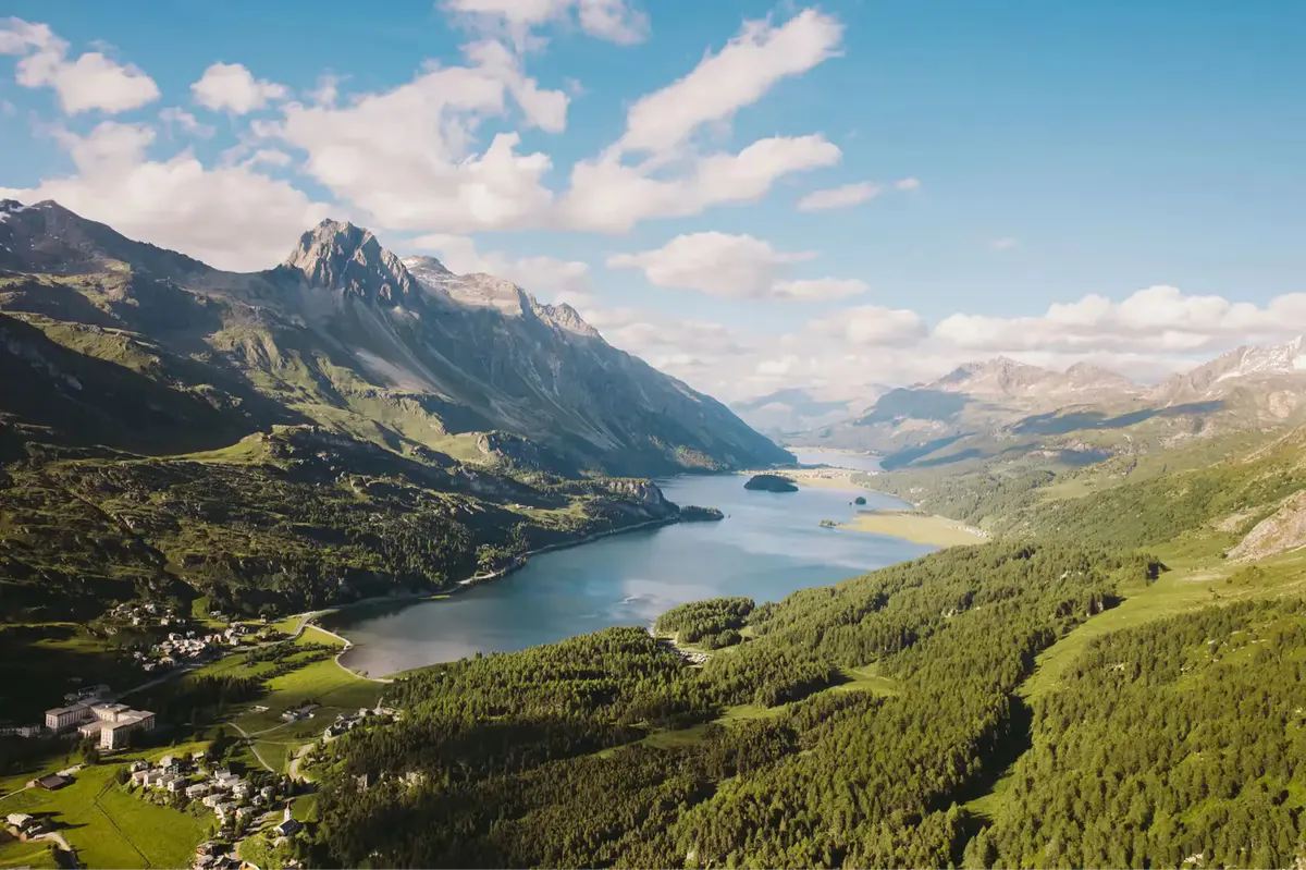 An aerial view of the lake surrounded by forested valleys and snow-capped peaks