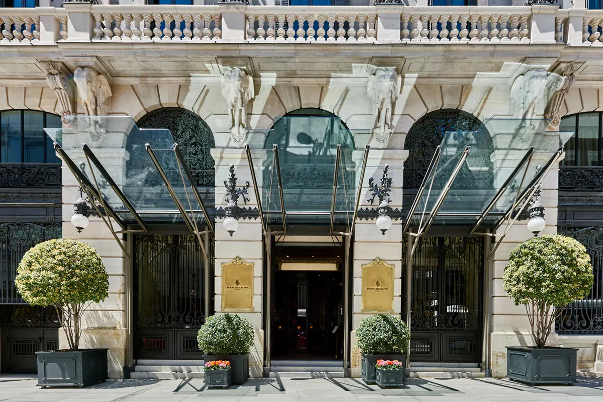 Black and glass entry doors with limestone archway and marble facade, flanked by topiary plantings