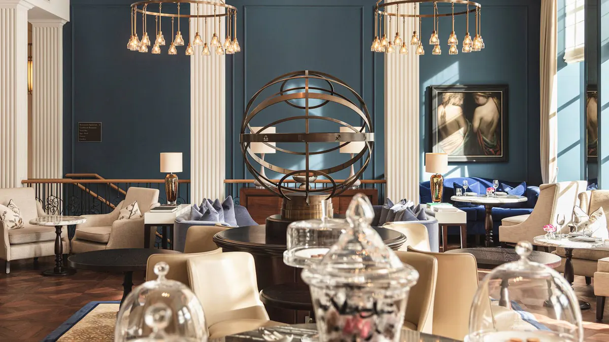 An elegant salon with blue walls, hanging gold light fixtures, marble columns, and modern sculptural art pieces