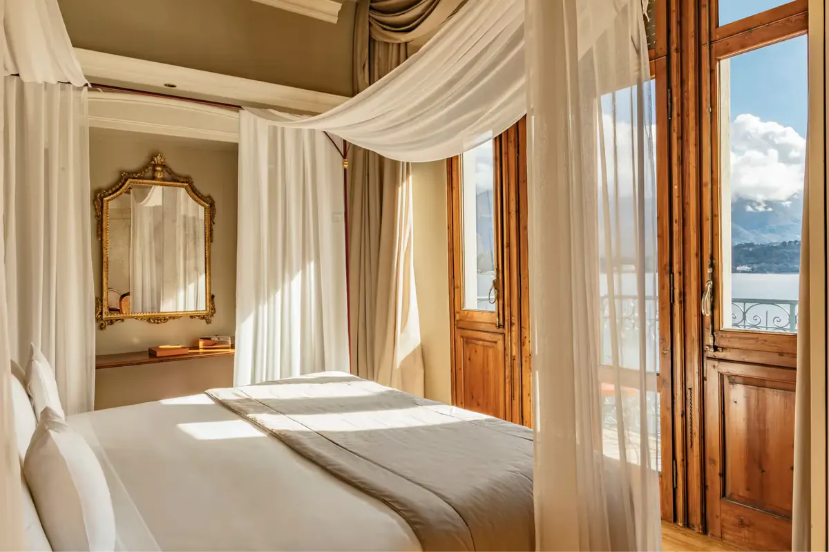 A suite bedroom with draped canopy bed, marble vanities, and mountain lake views
