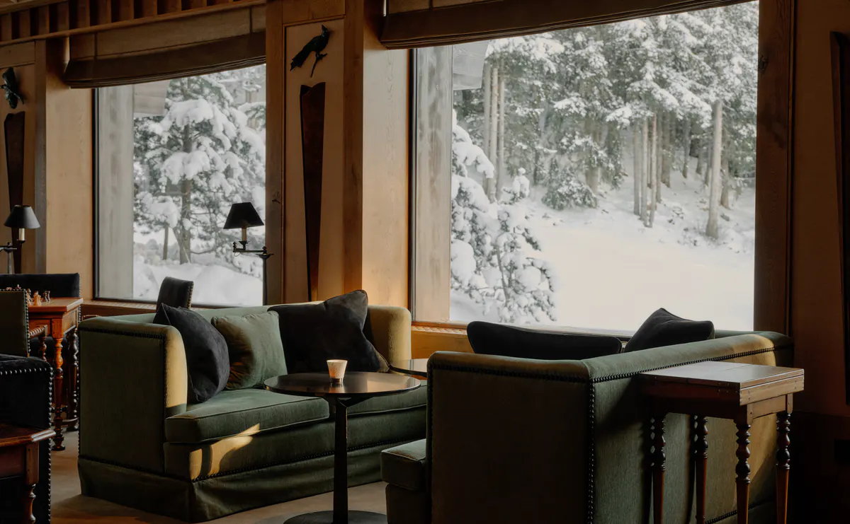 Lounge with deep green sofas and low tables overlooking the snowy village and ski slopes