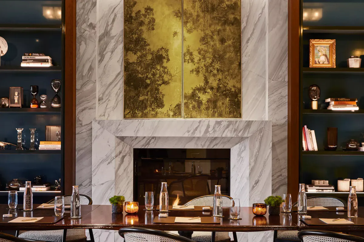 A fireplace with marble surround, gold leaf artwork, and built-in shelving with decor