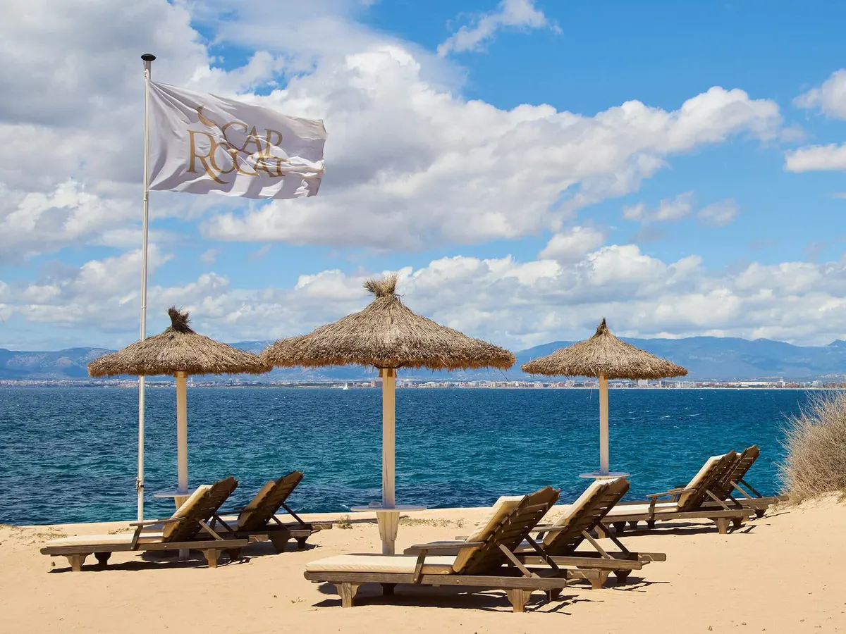 A private beach cove with thatched umbrellas and loungers on sand beneath clear skies