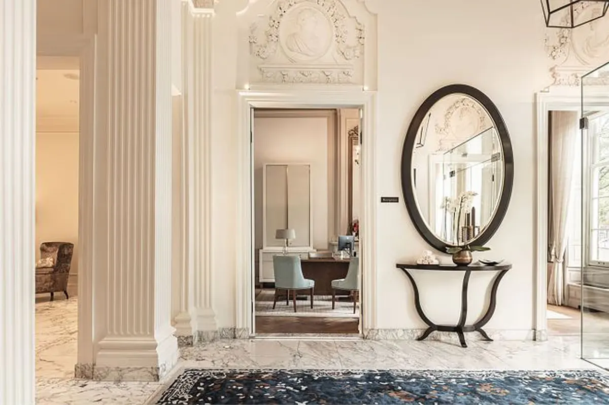 An entryway with fluted columns, arched mirrors, and a sculptural console table on marble flooring