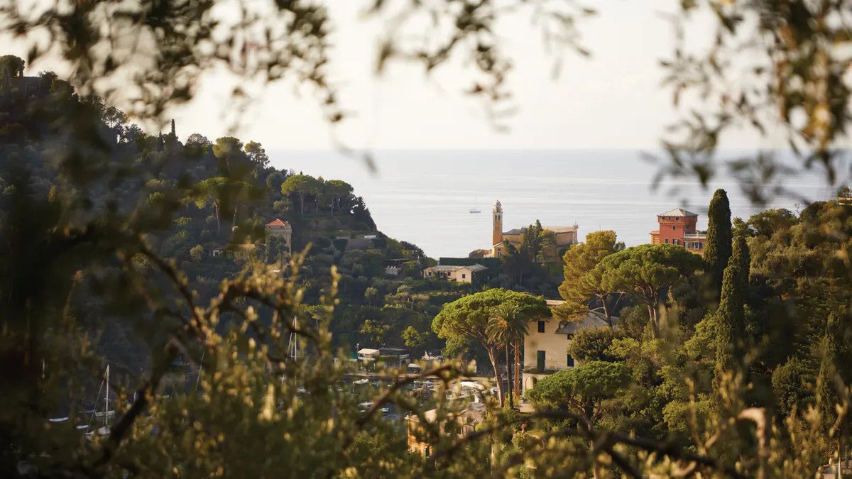 The hotel hillside surrounded by trees framing a distant sea view under pale sky