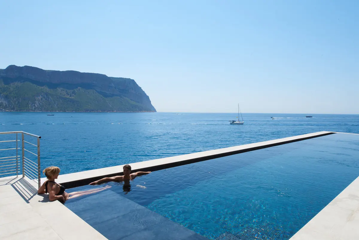 An infinity pool edge overlooking the sea, with the coastline and pine trees visible beyond