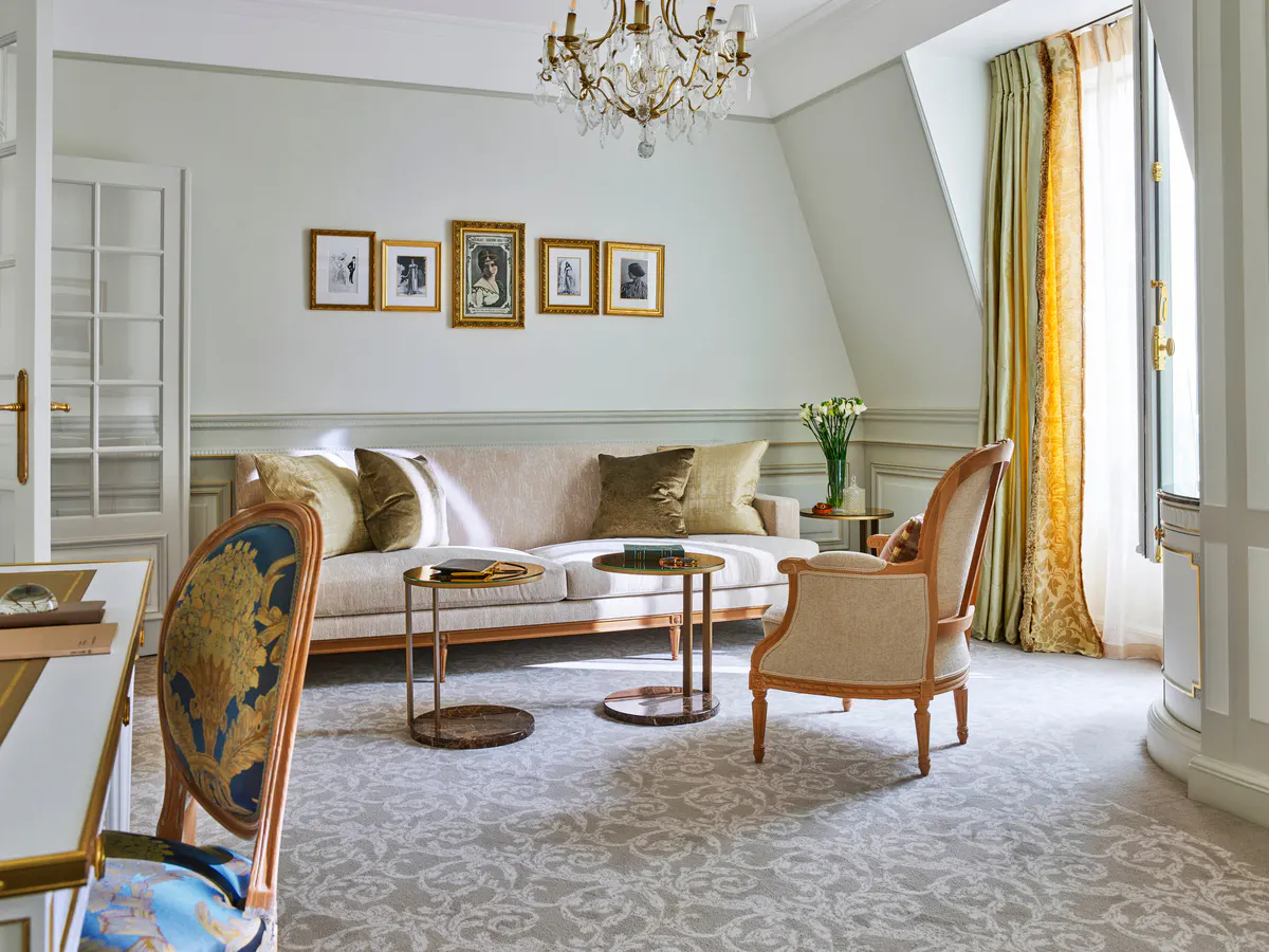 A sitting room in pale tones with sofa, chair, desk, and French doors to a balcony view