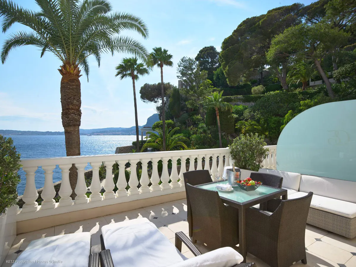 Palm trees frame a stone terrace with seating and views across the Mediterranean