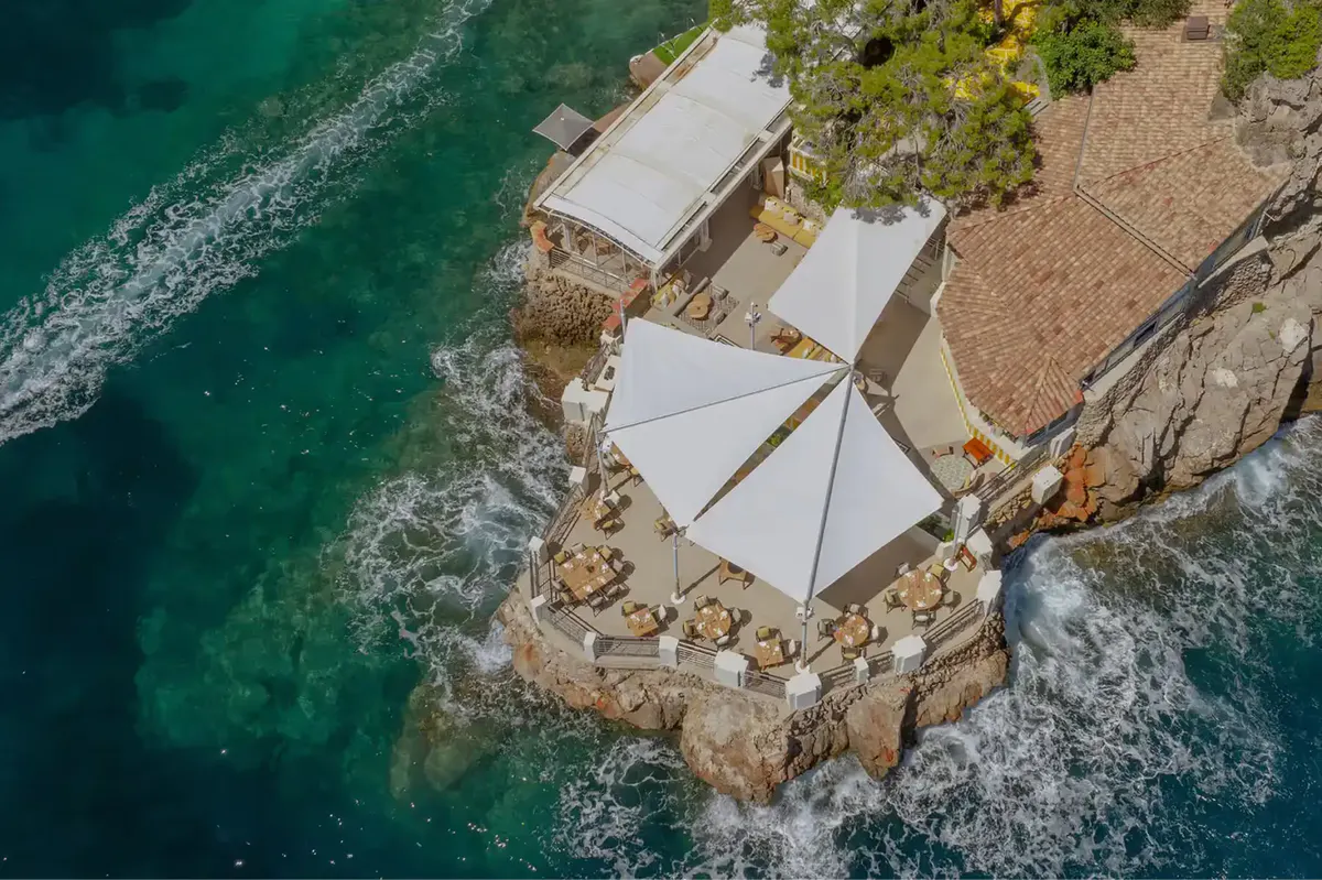 Cliff-side beach area with white umbrellas overlooking green Mediterranean water