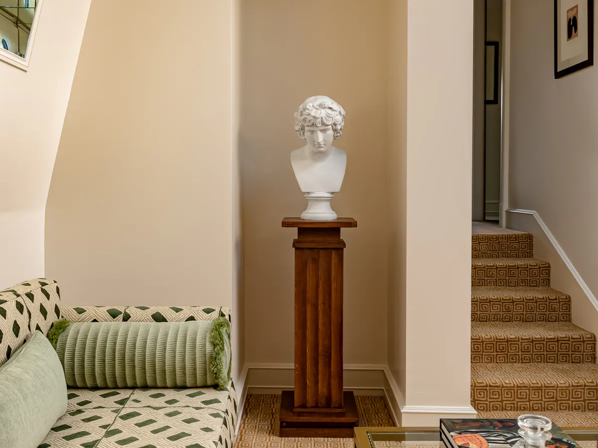 Hallway with sculptural marble bust on pedestal, cream walls, and classical archway entrance