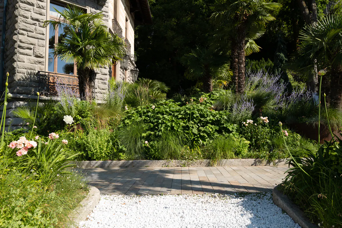 Shaded garden path with potted plants, flowering vines, and stone architecture