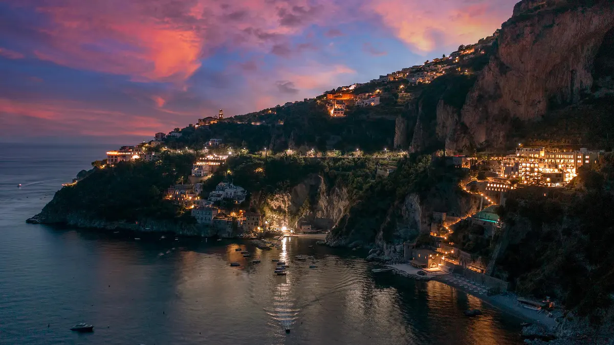 Property exterior at night with warm lighting against dramatic rocky coastline backdrop