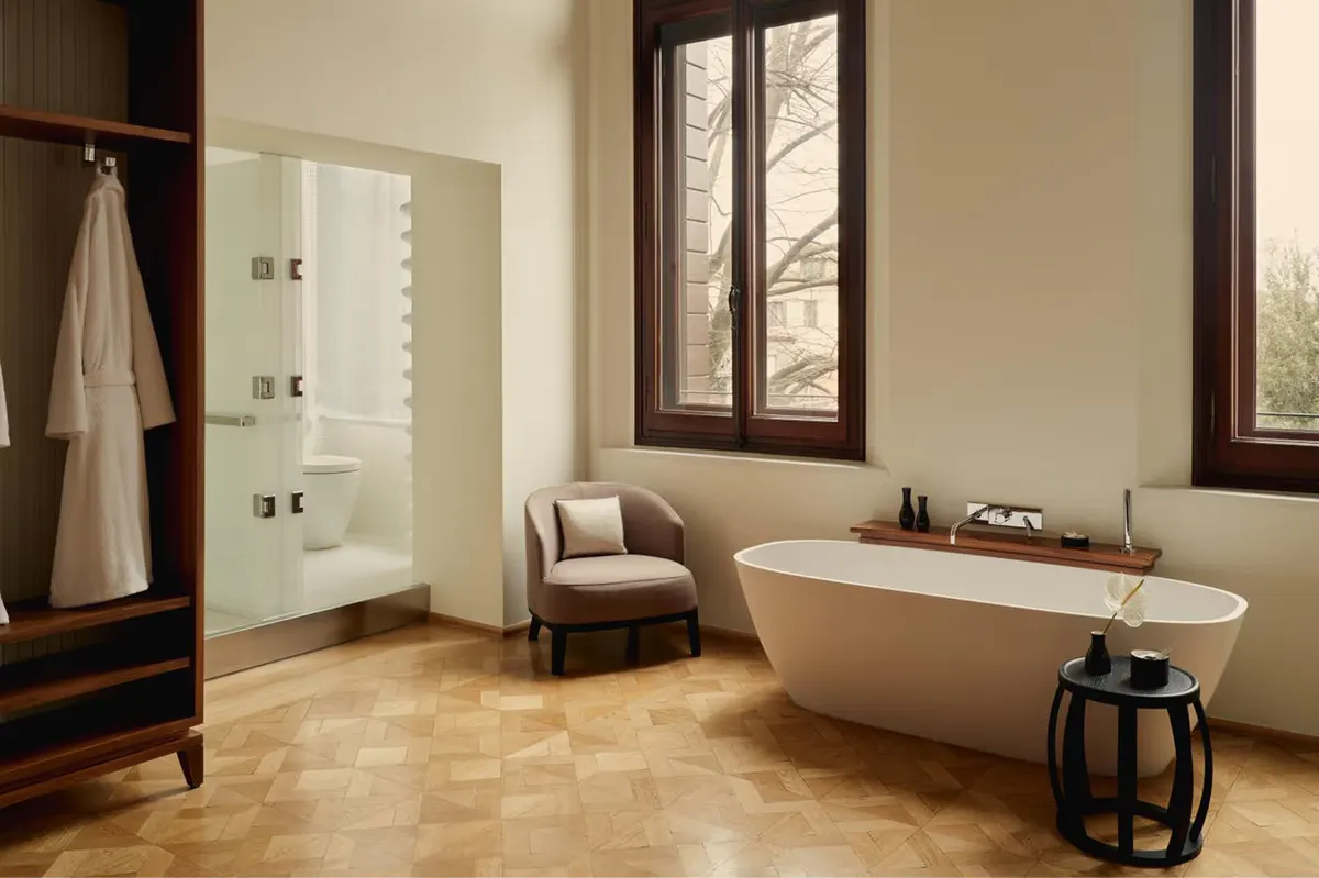 A spa bathroom with a freestanding white stone tub, glass-enclosed shower, and windows opening to green views