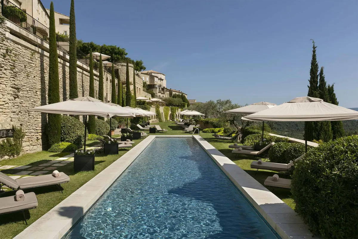 Rectangular pool with loungers and white umbrellas framed by stone columns