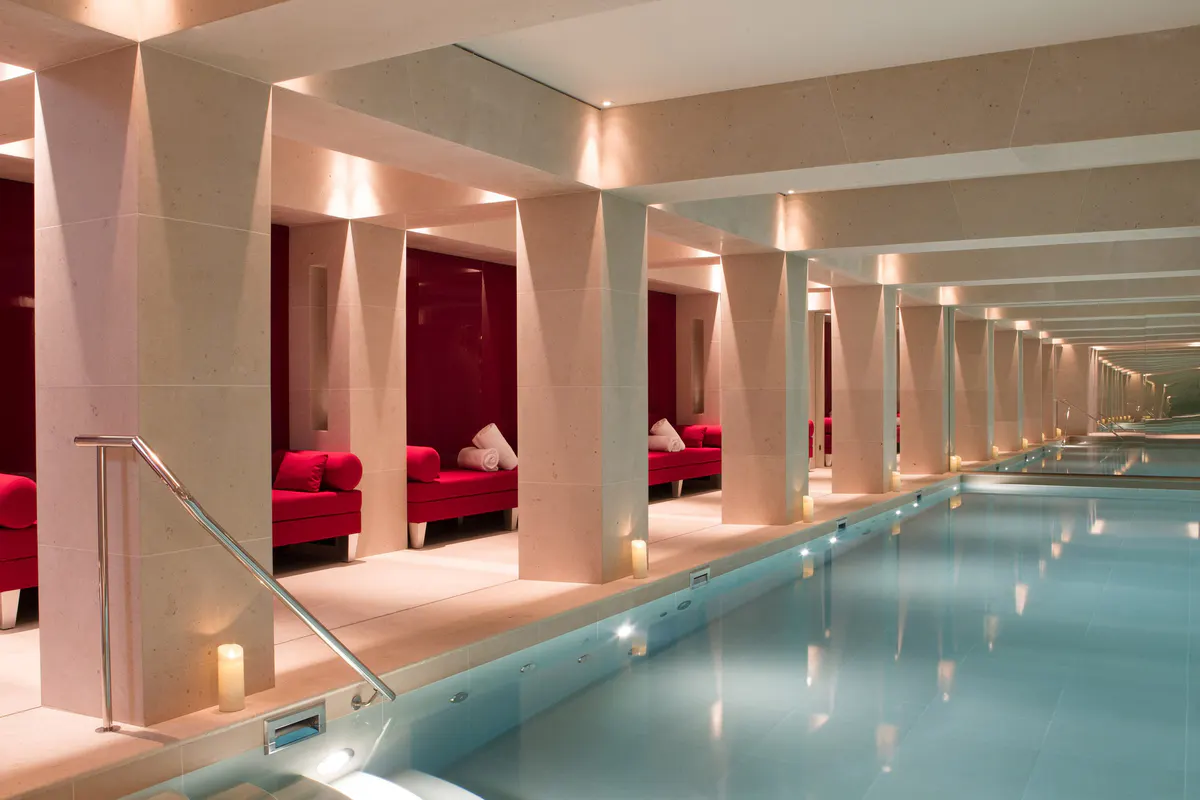 An indoor pool with red velvet seating alcoves and symmetrical warm lighting