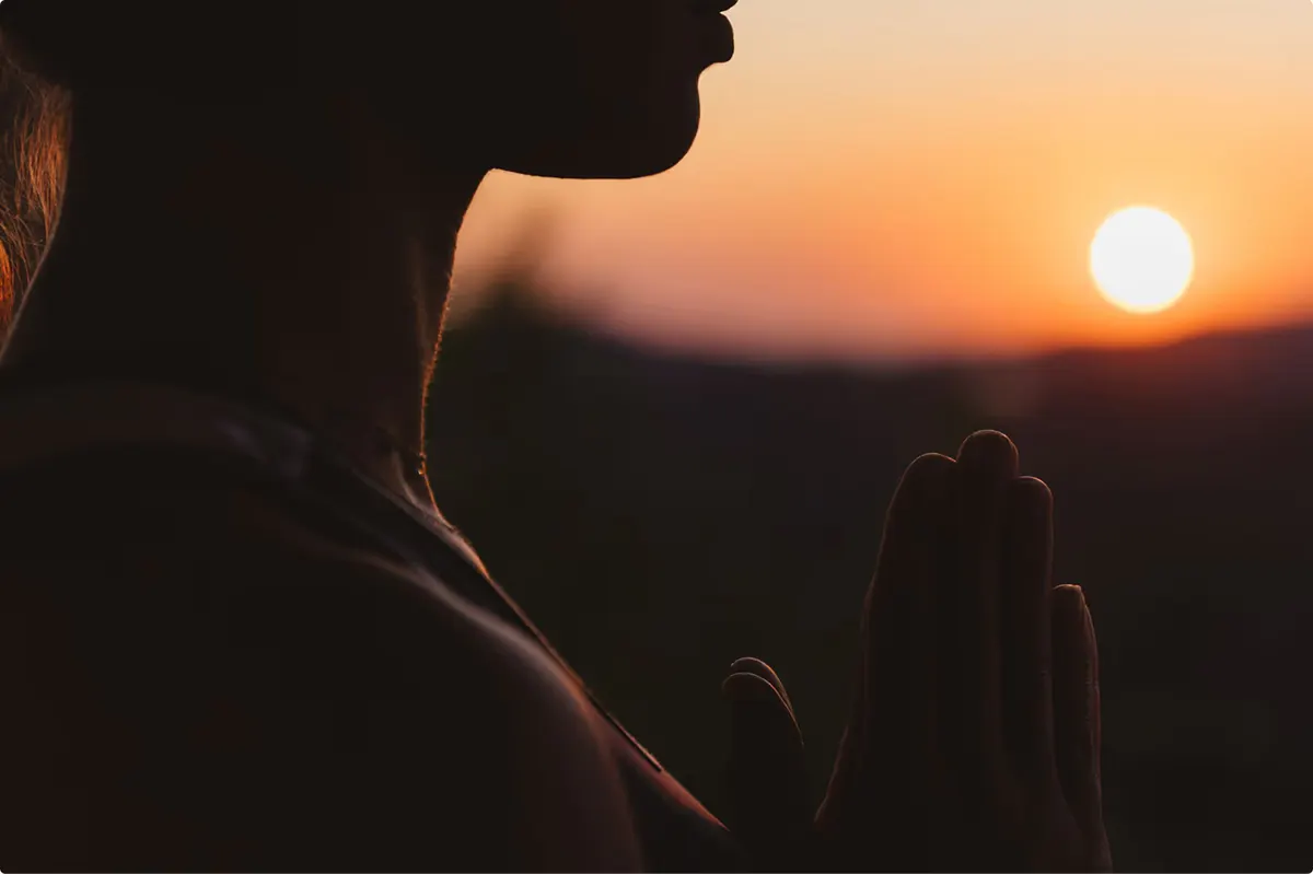 Person in meditation pose at dusk with mountain backdrop