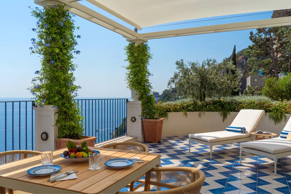 Furnished terrace beneath pergola with climbing ivy and seating overlooking the sea
