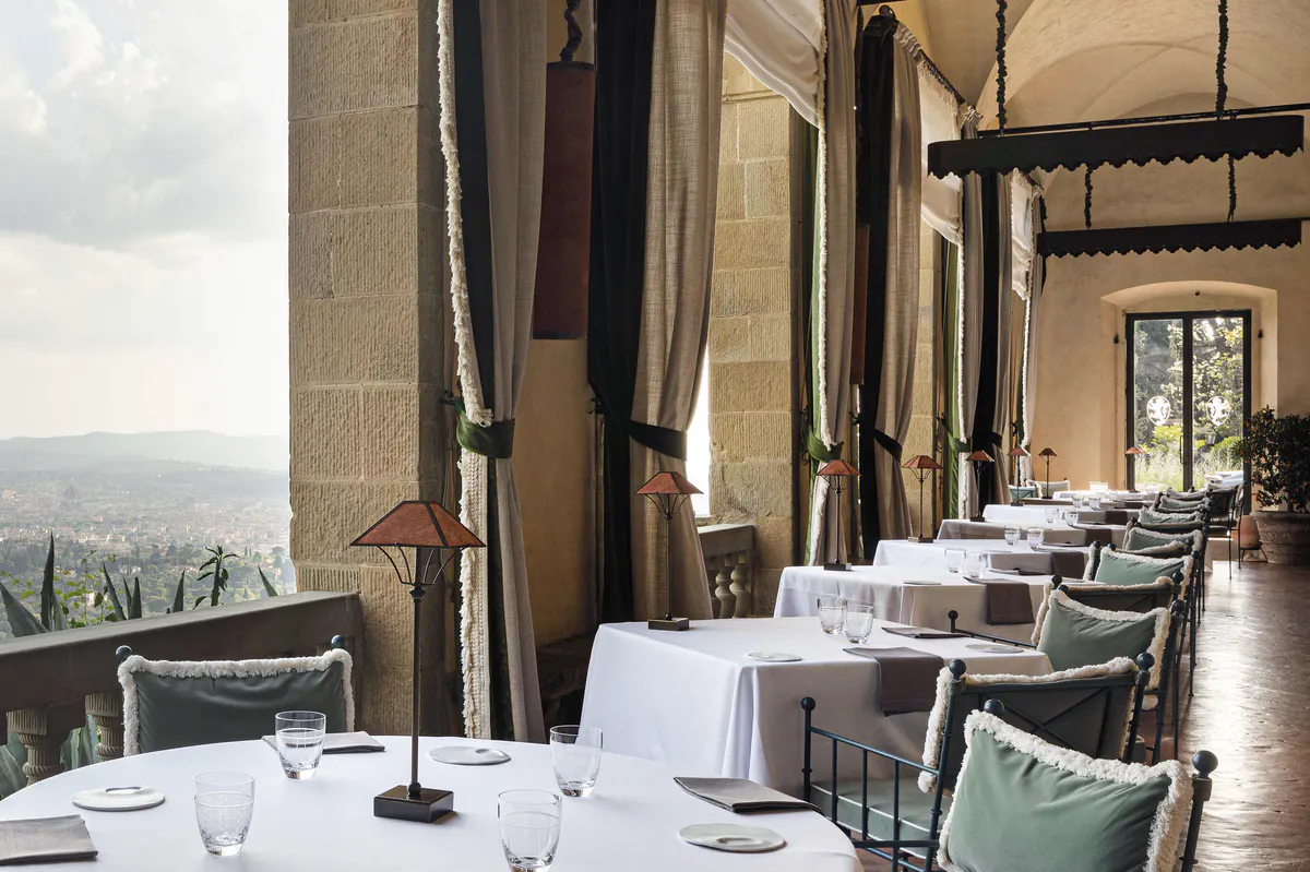 A formal dining room with tall columns, white tablecloths, and sweeping views to distant hills