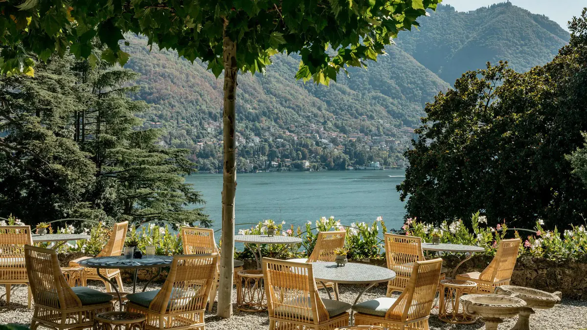 Garden dining area with rattan chairs, ancient tree, and lake mountains beyond